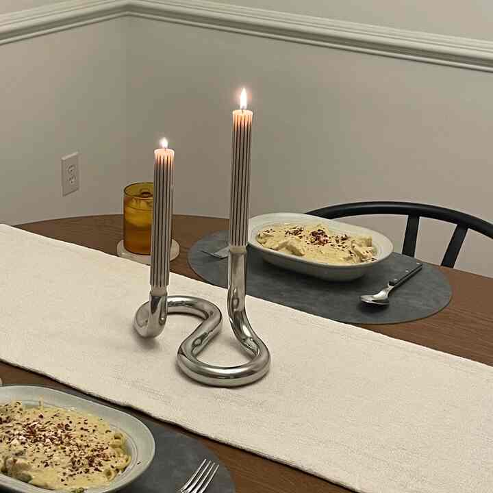 Brown dining table with white table runner in dining room featuring a central silver candle holder with lit candles creating cozy atmosphere