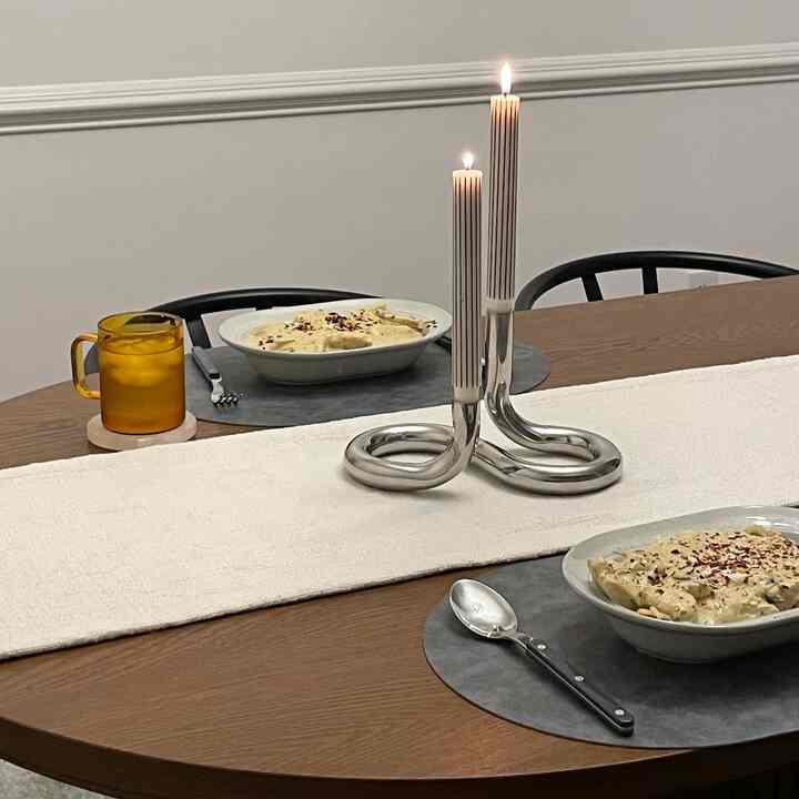 Modern dining room with brown wooden table, white table runner, lit candles, and two serving dishes for two people