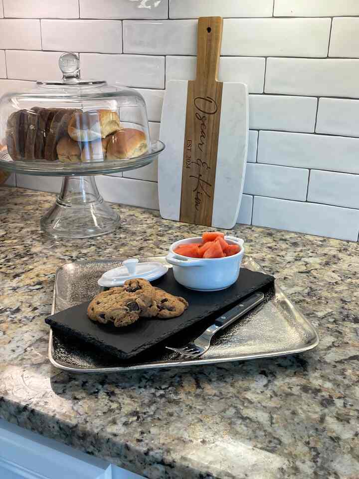 White tiled backsplash and brown cutting board on kitchen countertop, white mini cocotte with cookies and watermelon creating a home cafe vibe