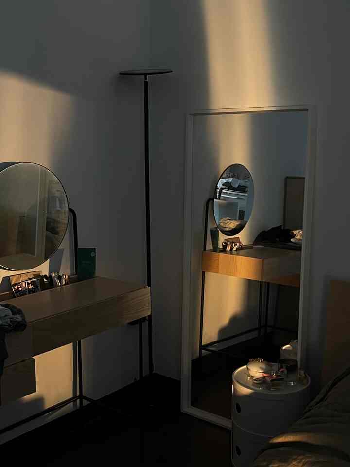 Modern minimal bedroom corner with white walls, large mirror, and wood-tone vanity arranged neatly
