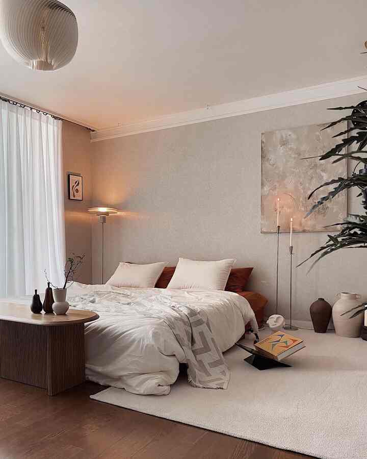 Warm beige and natural tone bedroom featuring a low bed with bedding, wooden bench, soft lighting, and calming minimalist decor
