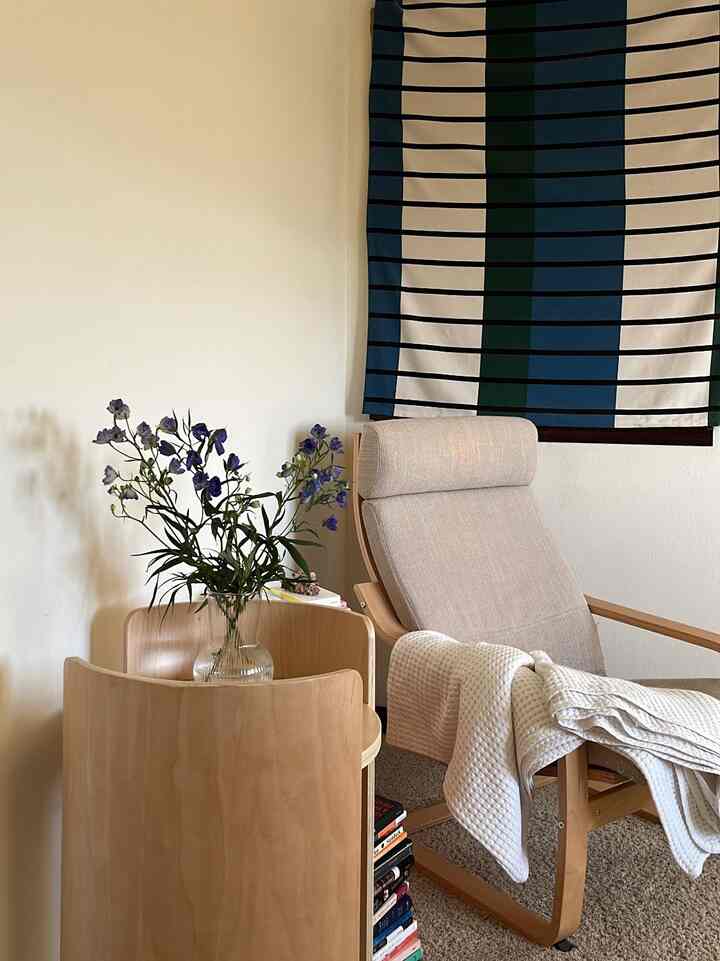 Natural-toned bedroom corner featuring a beige armchair and a wooden side table with a vase of flowers, creating a cozy atmosphere