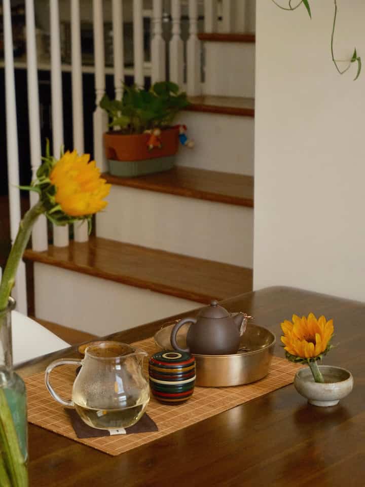 Natural wood-toned dining room featuring a tea set and sunflowers placed on a wooden table, creating a cozy home cafe atmosphere