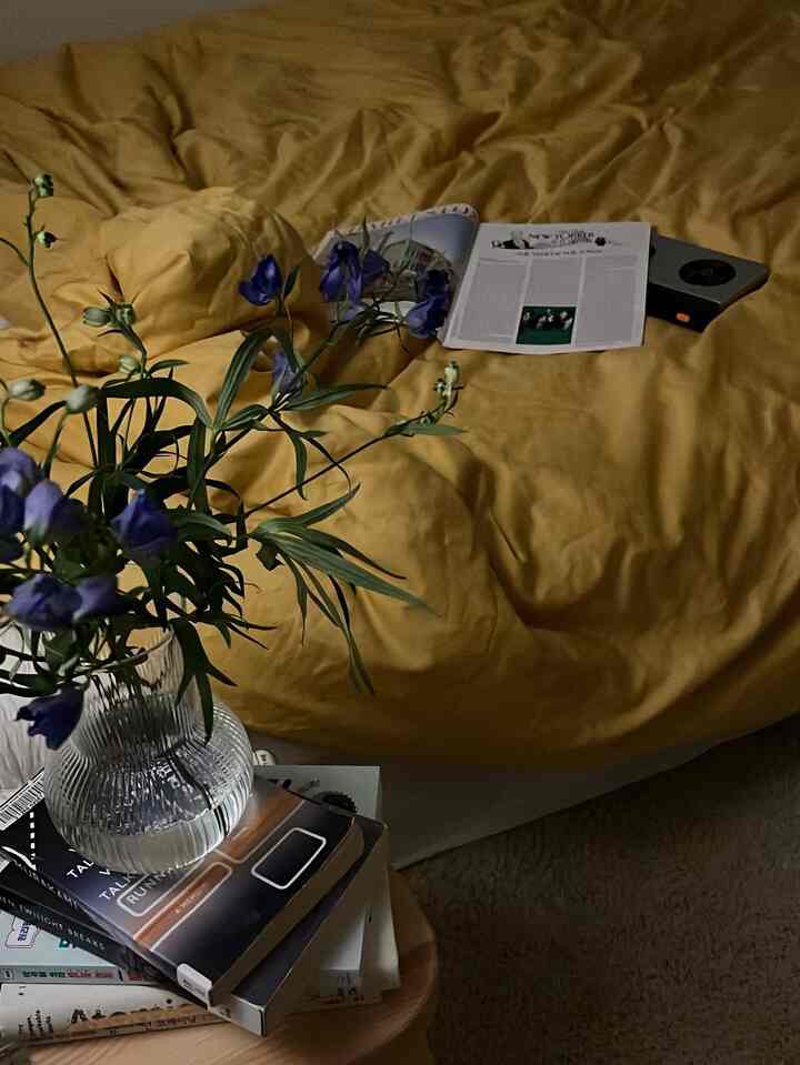 Bedroom with yellow duvet cover bed featuring a glass vase with blue flowers and books on a nearby table, creating a cozy atmosphere
