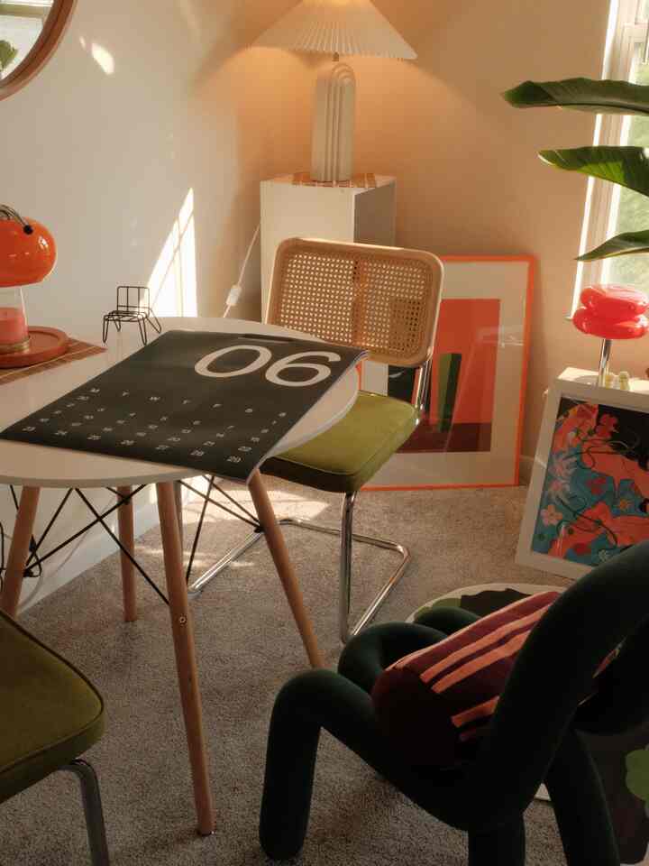 Beige-toned dining room with carpet, green chairs, table lamps, and posters creating a cozy cafe style interior