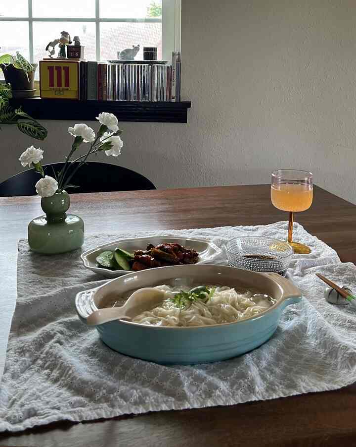 Natural and white toned dining room featuring a wooden table set with dishes and a vase with flowers, creating a cozy atmosphere