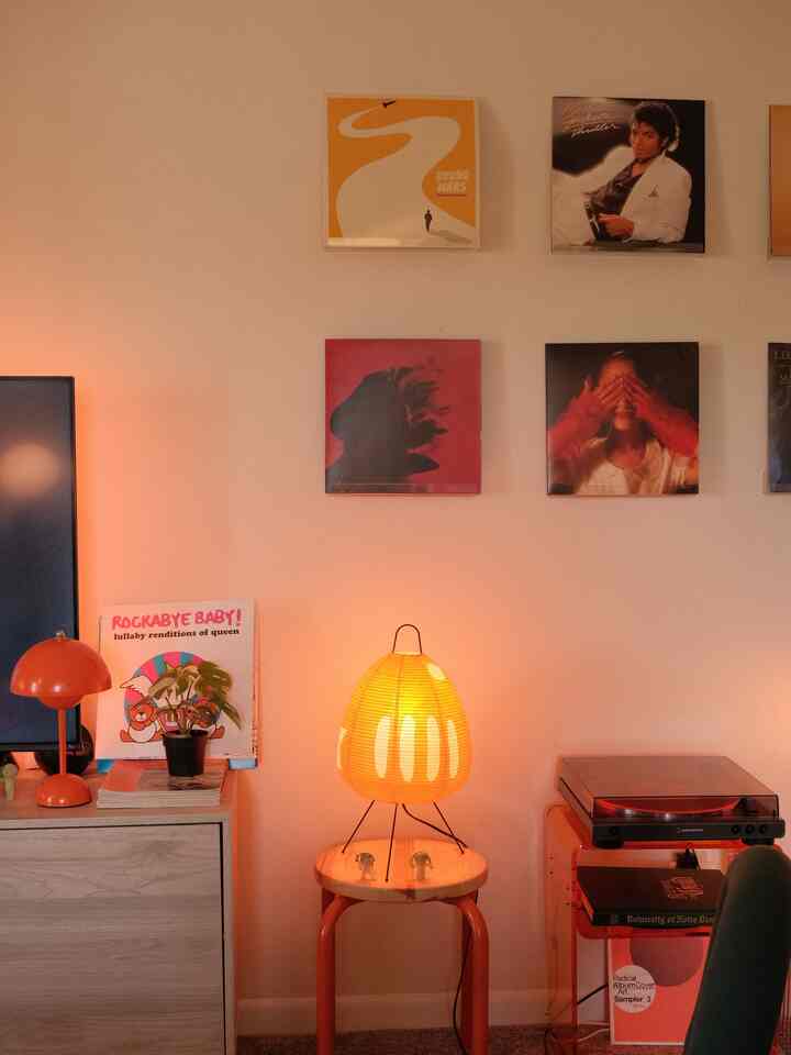 Warm orange-lit interior featuring vintage vinyl covers displayed on the wall, audio equipment, and a stool creating a cozy home office vibe