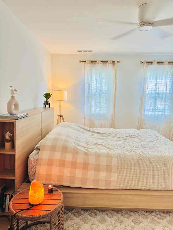 Beige and wood tone bedroom featuring a bed, curtains, and floor lamp with a cozy and natural atmosphere