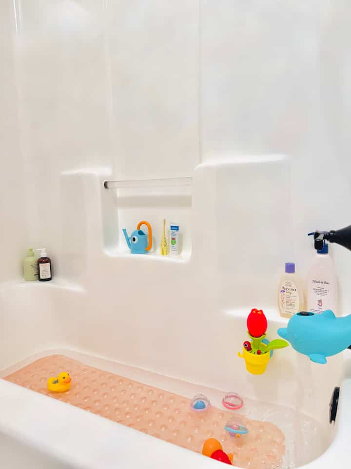 Natural tone bathroom featuring a baby bathtub with colorful toys and a non-slip mat, creating a safe baby bathing space