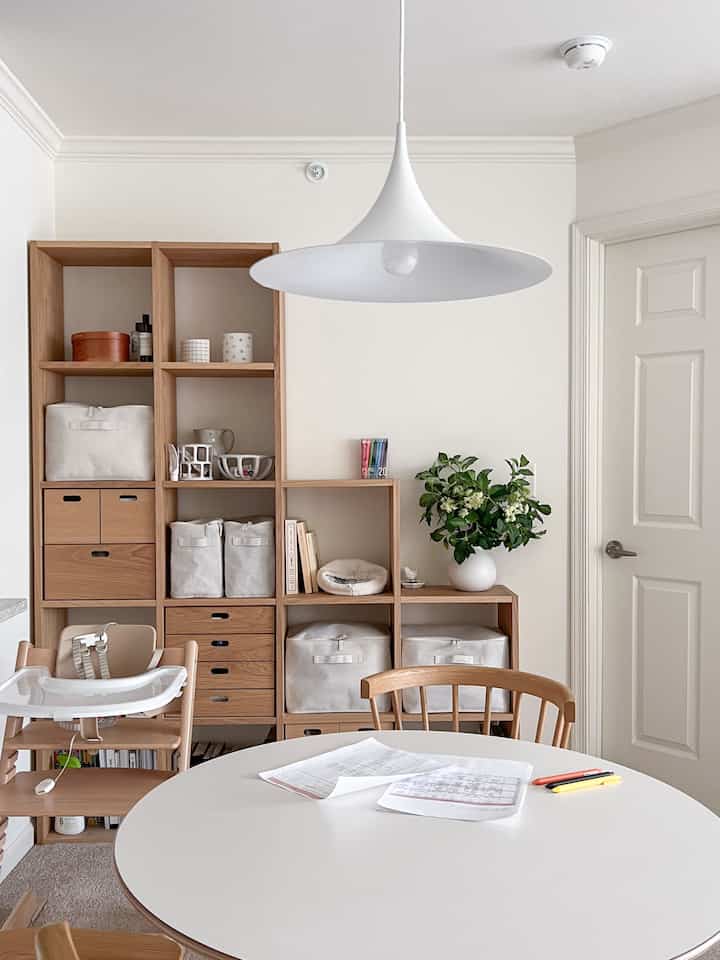 White and wood-tone living room featuring wooden shelves and a baby high chair, creating a clean and cozy space