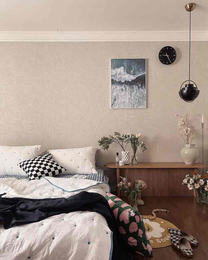 Beige-walled mid-century modern bedroom featuring white bedding, cushions, a wooden bench, and decorative vases with flowers