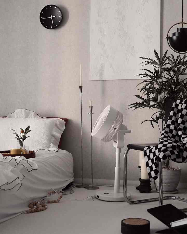 Light gray and white toned bedroom featuring a bed, Thonet chair, standing fan, and checkered throw blanket with a modern clean atmosphere
