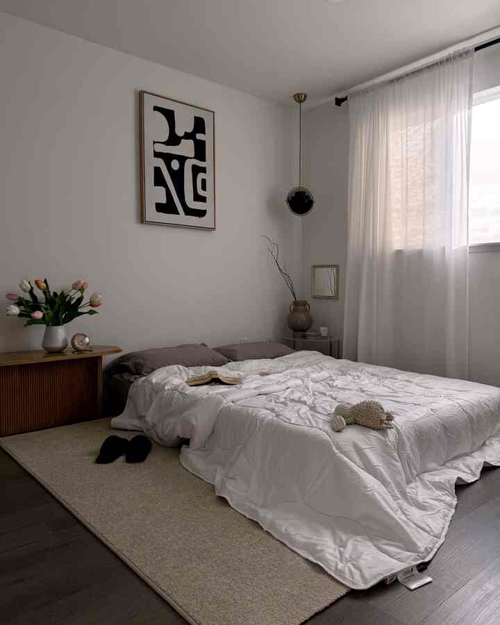 White and natural tone bedroom featuring a bed, nightstand, curtains, and vase, creating a minimal and calm atmosphere