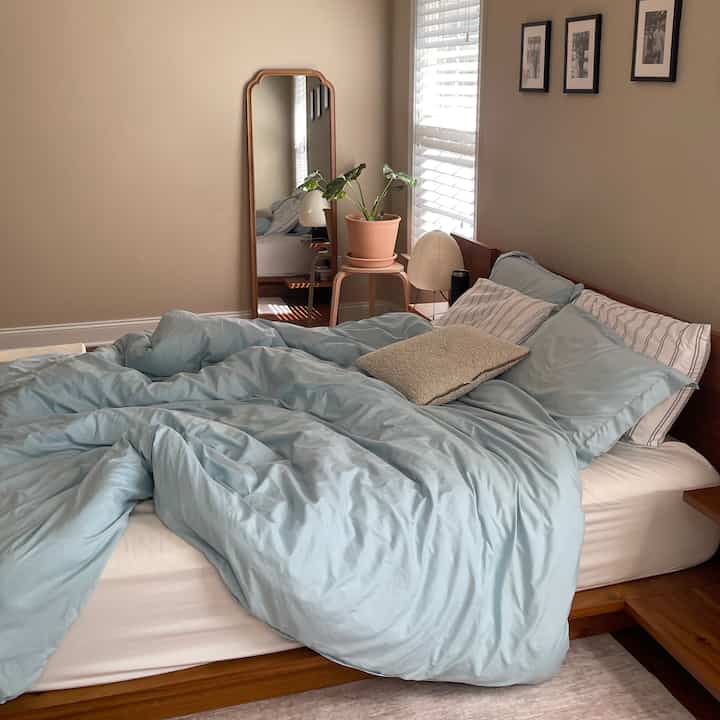 Beige walls with natural wood bed and pastel blue bedding create a cozy natural bedroom