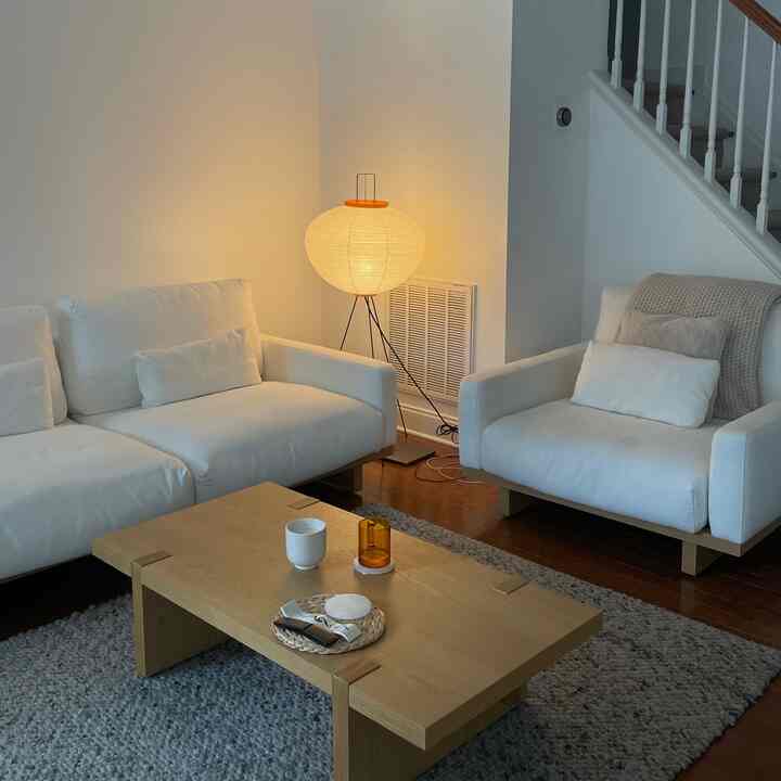 White and wood-tone two-person living room featuring minimal Japandi style, simple furniture layout with warm floor lamp creating cozy atmosphere