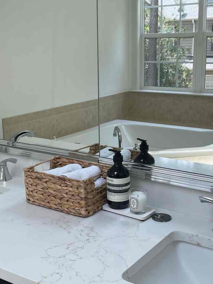 White and beige toned bathroom featuring a marble countertop with a towel basket, diffuser, and candle creating a clean atmosphere