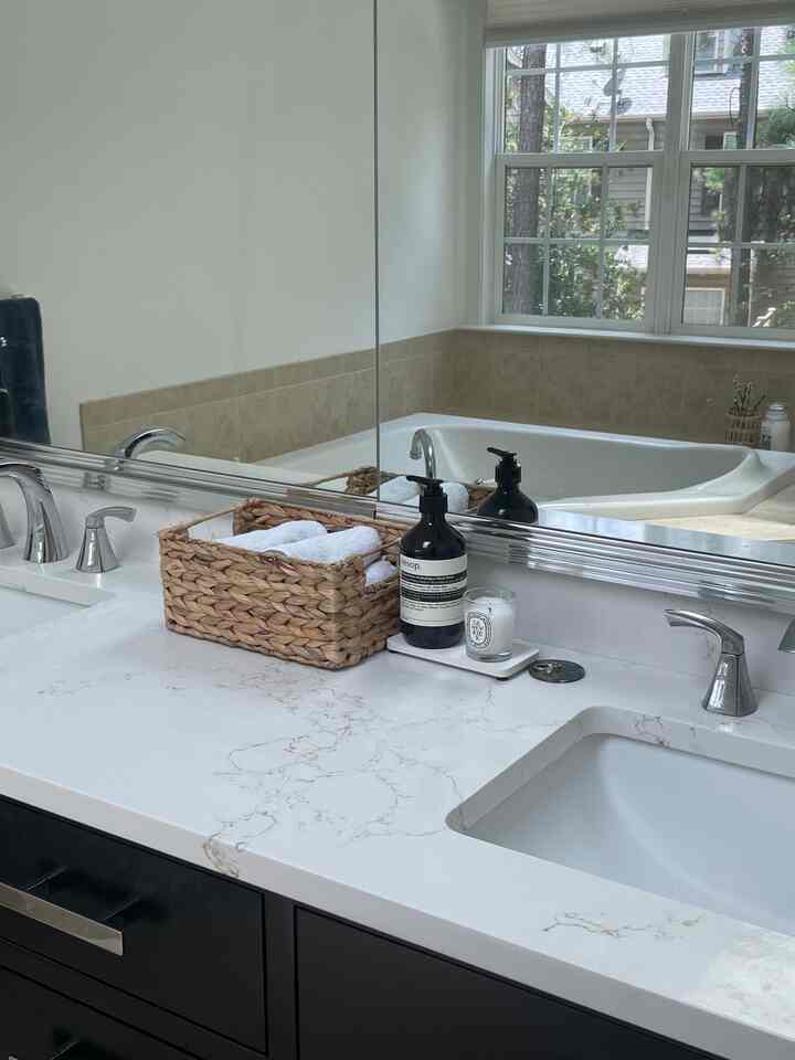 Minimal bathroom sink with white marble countertop, brown wicker basket, and large mirror reflecting a serene natural view
