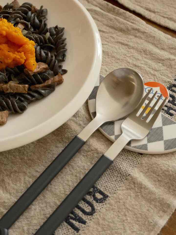 Beige kitchen towel featuring black-handled cutlery and a white plate as kitchen accessories