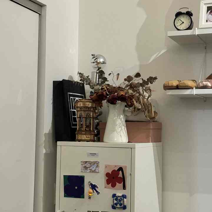 A small corner room in white and beige tones featuring a cabinet with a vase and decorative items, creating a simple and cozy atmosphere