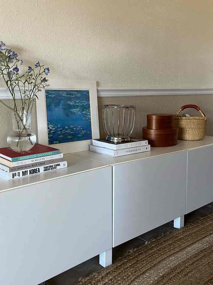 Natural-tone walled entrance featuring white storage cabinets topped with a vase of flowers, books, and baskets creating a warm atmosphere