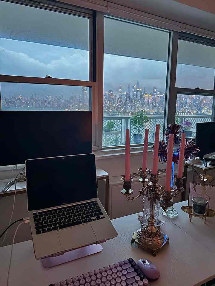 White and blue toned home office with pink candles on desk, overlooking a city skyline from balcony windows