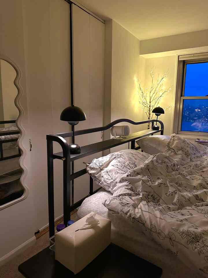 White-toned bedroom with black metal bed frame, cozy mood lighting from lit birch lamp, and comfortable bedding