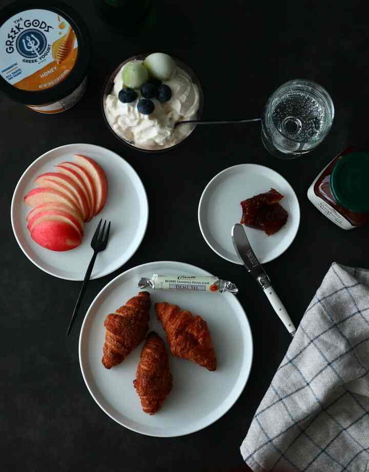 White and black toned dining table featuring croissants, apple slices, yogurt, and jam creating a breakfast setting