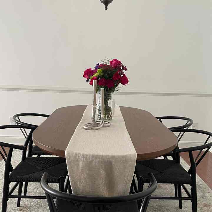 Natural modern dining room with brown wooden table and black chairs, featuring a beige table runner and vibrant red flower vase centerpiece