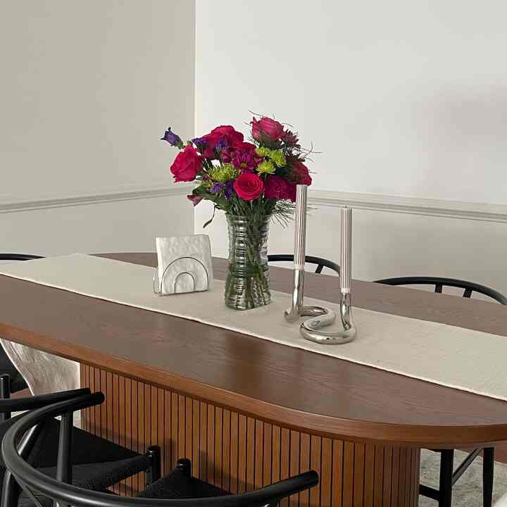 Natural color dining room with wooden dining table, featuring a central vase of flowers and silver candle holders in a minimalistic setting