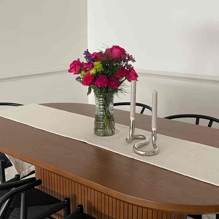 Brown wooden dining table with white table runner, pink flower bouquet, and silver candle holders in a clean dining room