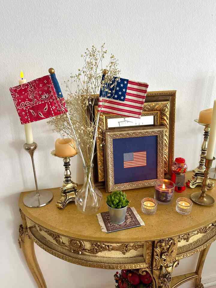 Cozy space with white walls and a gold vintage table featuring a vase, picture frames, candles, and a plant