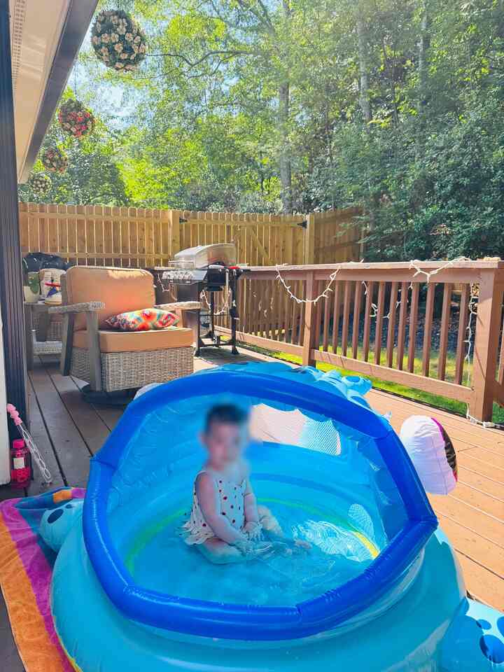 Bright blue outdoor balcony featuring inflatable kiddie pool, swivel patio chair, and grill with a natural atmosphere