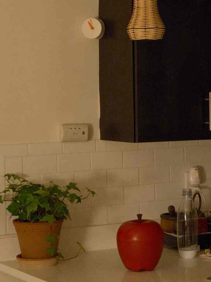 White tiled backsplash and dark cabinetry kitchen featuring a green plant and a red apple-shaped container, creating a cozy atmosphere
