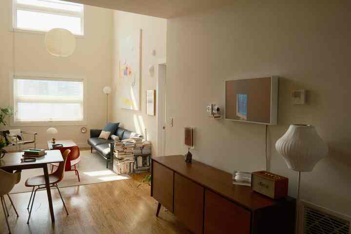 Bright modern living and dining space for four featuring white walls, wood tone flooring, a black sofa, and a wooden sideboard with cozy ambiance