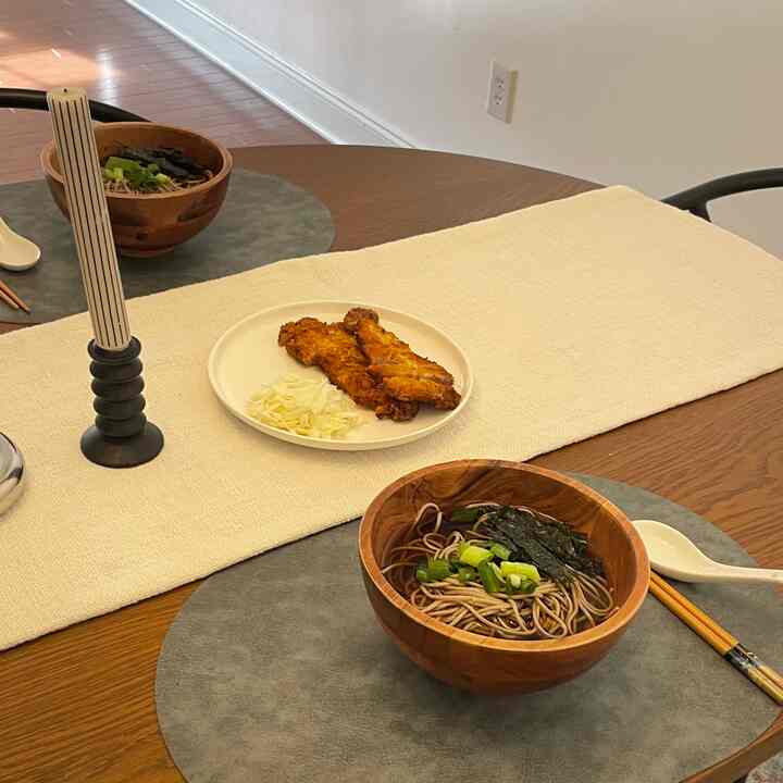 Natural wood tone dining room with a dining table featuring wooden serving bowls, fried food on a white plate, and a white table runner creating a cozy atmosphere