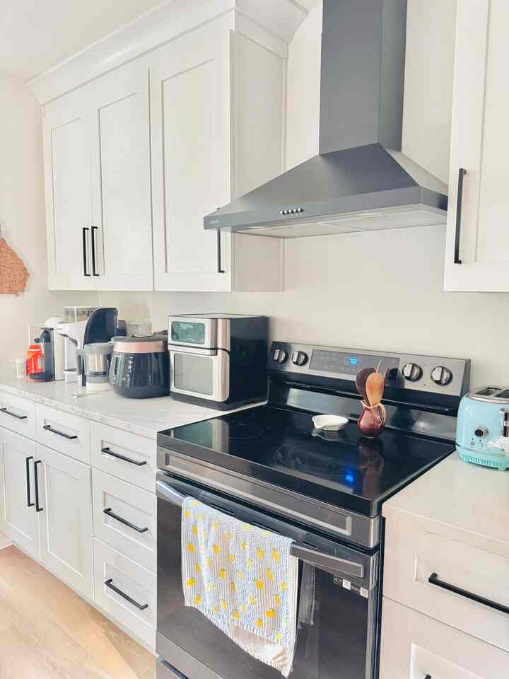 White-toned kitchen featuring a black electric stove and various neatly arranged kitchen appliances