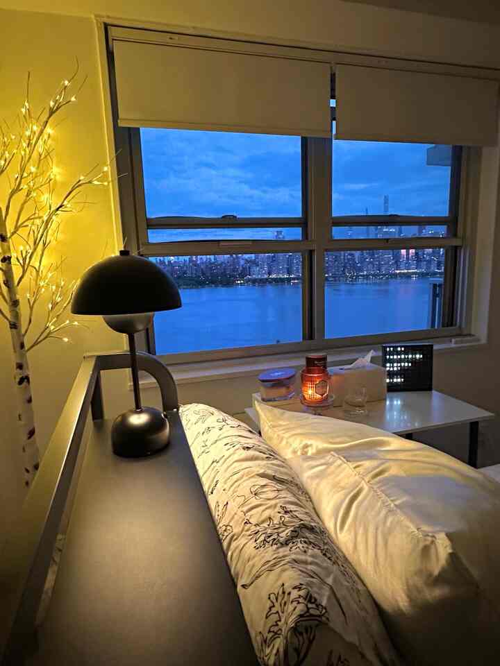 Warm yellow and white toned bedroom featuring a bed with pillows, table candles and a lamp creating cozy ambience