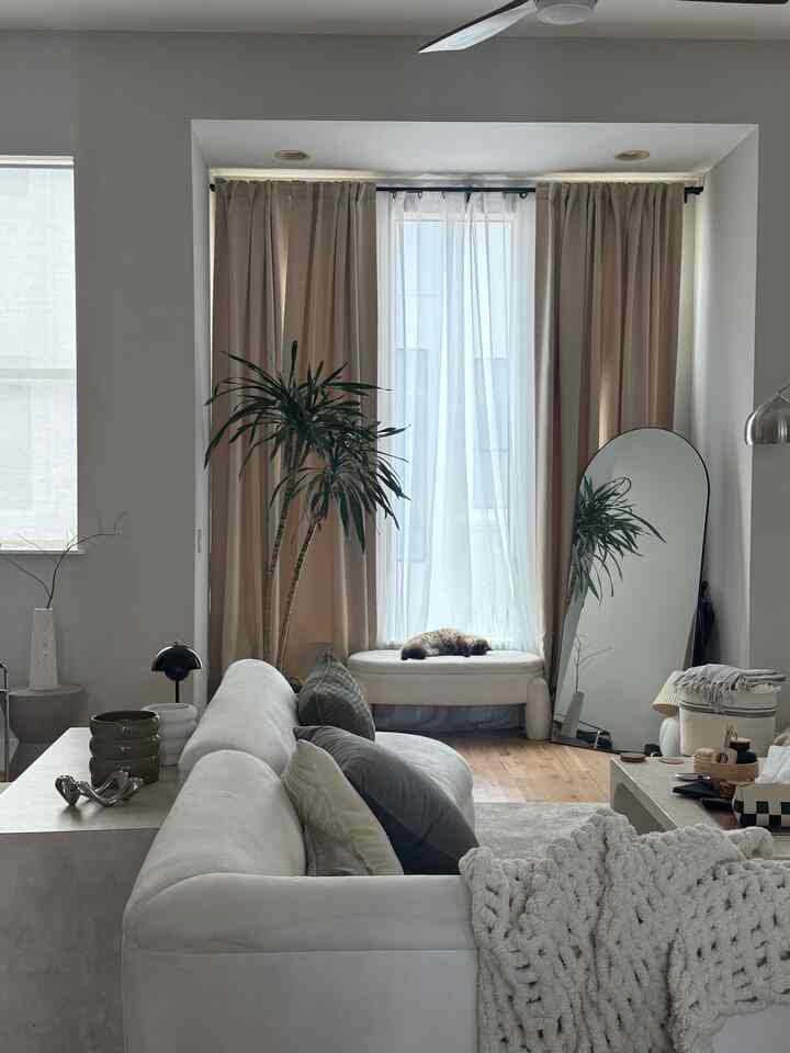 Bright white and beige toned living room featuring a large sofa with cushions and a cat sleeping by the window, creating a cozy atmosphere