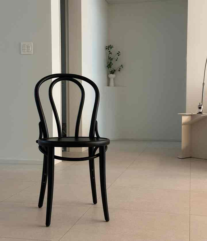モノトーンの狭い部屋に、中央に黒い木製のアームチェアが配置されたミニマルで清潔感のあるインテリア