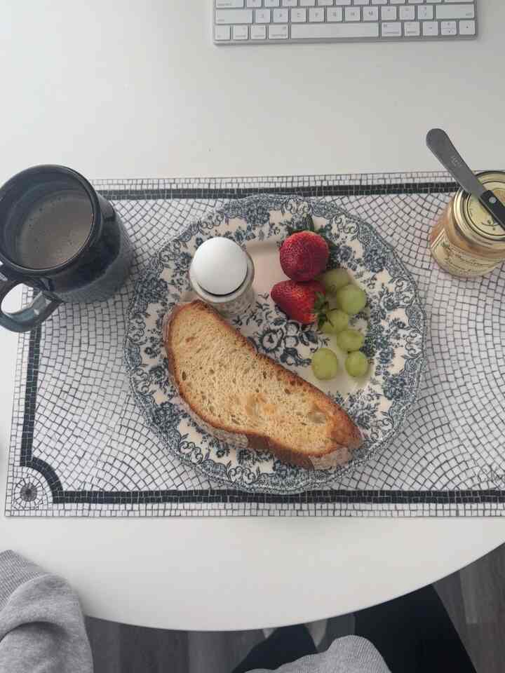 White-toned kitchen table featuring a floral plate with breakfast and a coffee mug in a calm morning setting