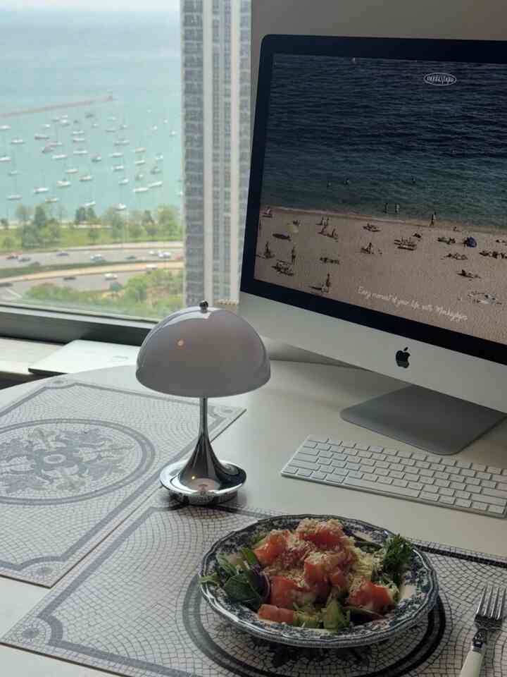 White and blue toned kitchen desk featuring an iMac, table lamp, and salad plate in a neat home office setting