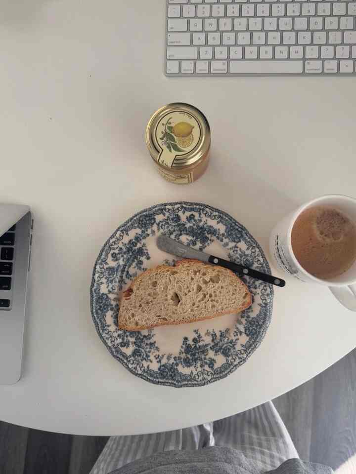 White-toned desk featuring bread and coffee next to a laptop, creating a cozy home cafe setting