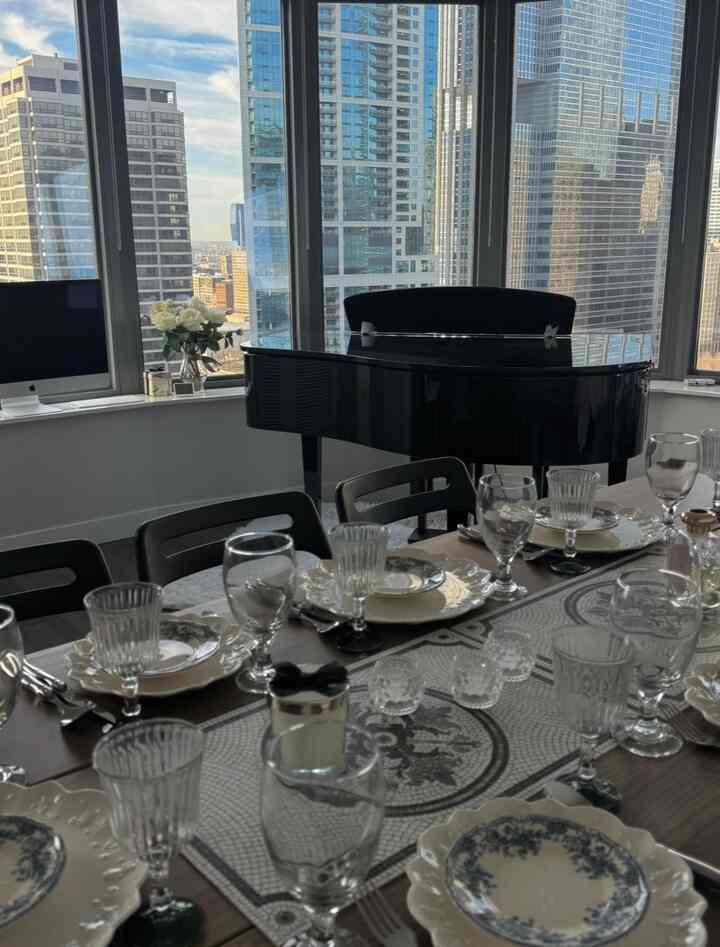 Modern living and dining room in white and black tones, featuring a black grand piano and a meticulously set dining table