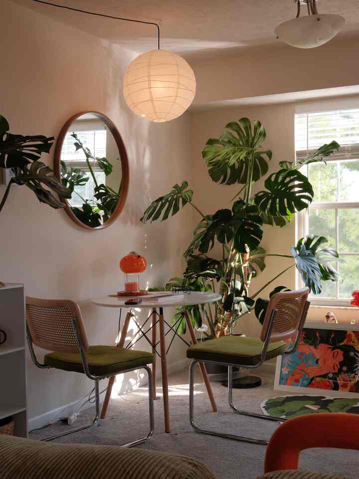 Beige-toned natural corner space featuring Monstera plant, round wall mirror, small round table and armchairs in a cozy home cafe setting