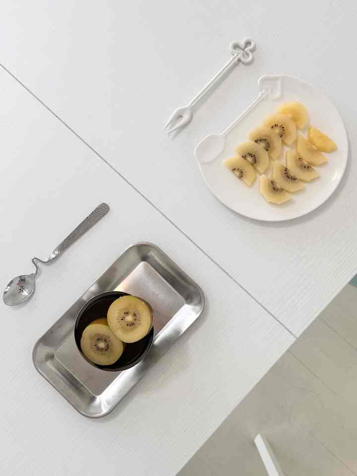 A clean and minimal home cafe scene featuring white and silver tones with kiwi slices on a dessert plate placed on a white table