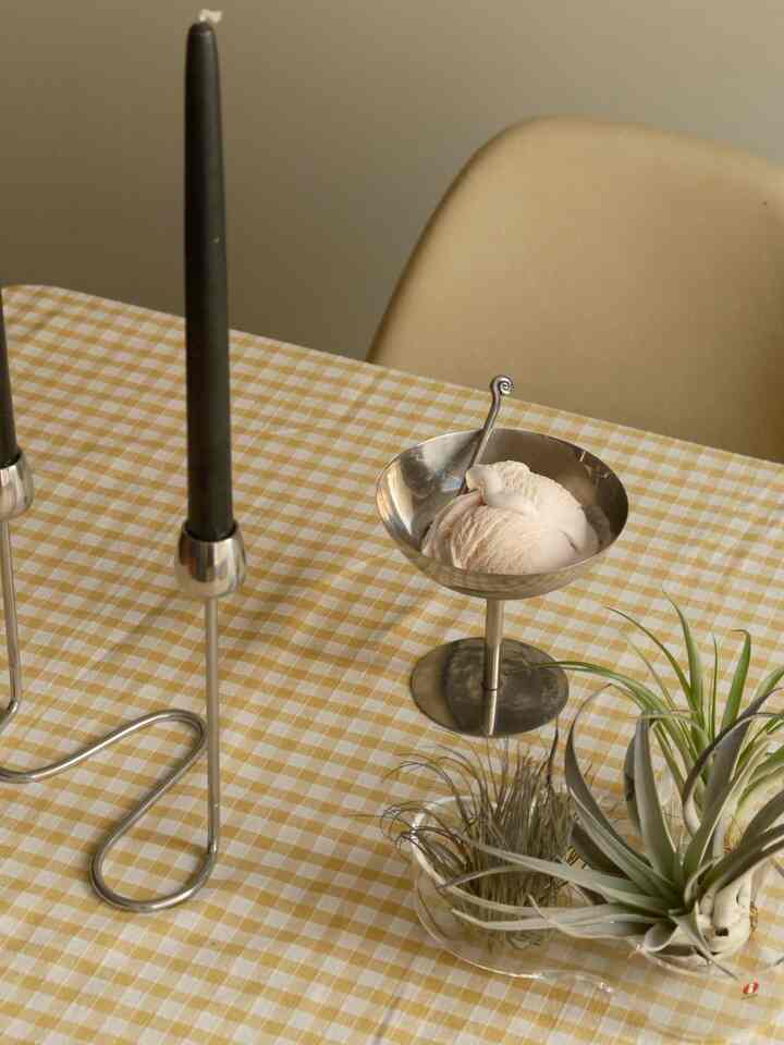 Warm brown and yellow toned dining table with silver ice cream bowl, black candlesticks, and beige dining chair in cozy setting