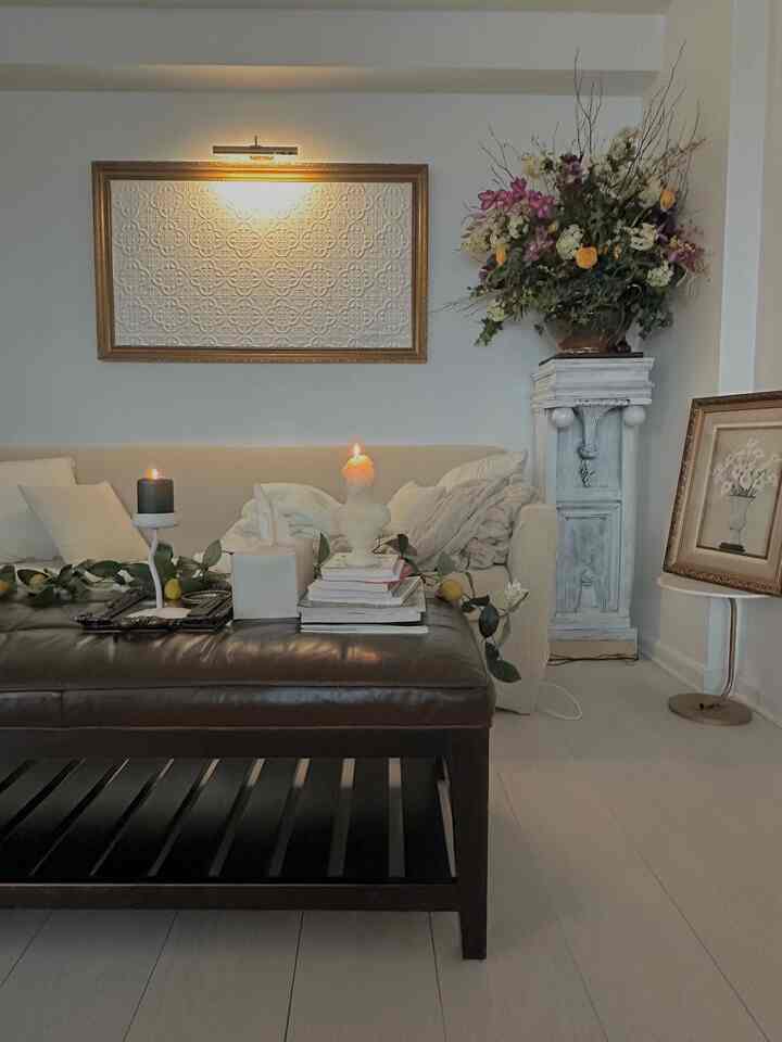 Natural-tone living room with ivory sofa and dark brown ottoman, featuring wall sconce lighting and candles creating a romantic ambiance