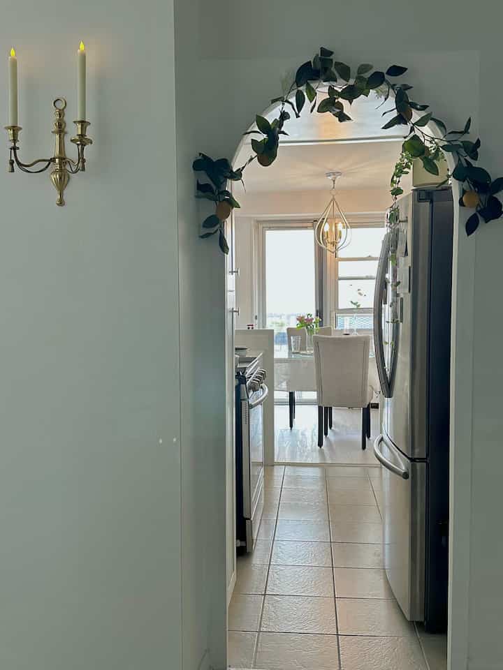 White and silver-toned kitchen entrance featuring lemon garland arch and gold wall candle sconce, creating a cozy summer interior vibe