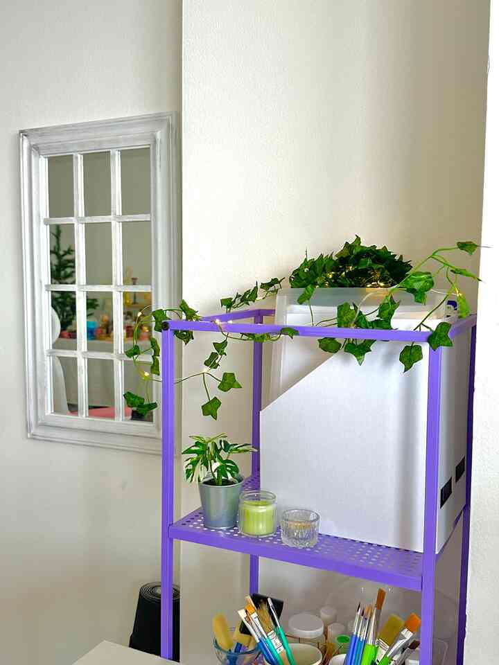 Storage space with purple metal shelving holding plants and candles against a white wall