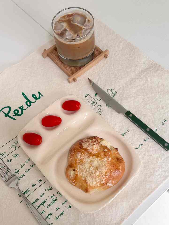 Beige kitchen towel table setting with iced coffee, bread, and cherry tomatoes in a simple home cafe style